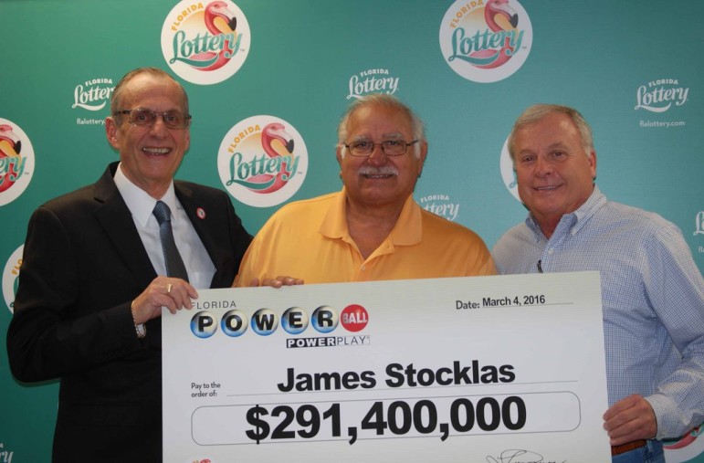 Barry Bartakovits (right) and James Stocklas (center) hold a check representing their Powerball winnings along with a Florida Lottery official Friday. A third local resident will also share the prize.