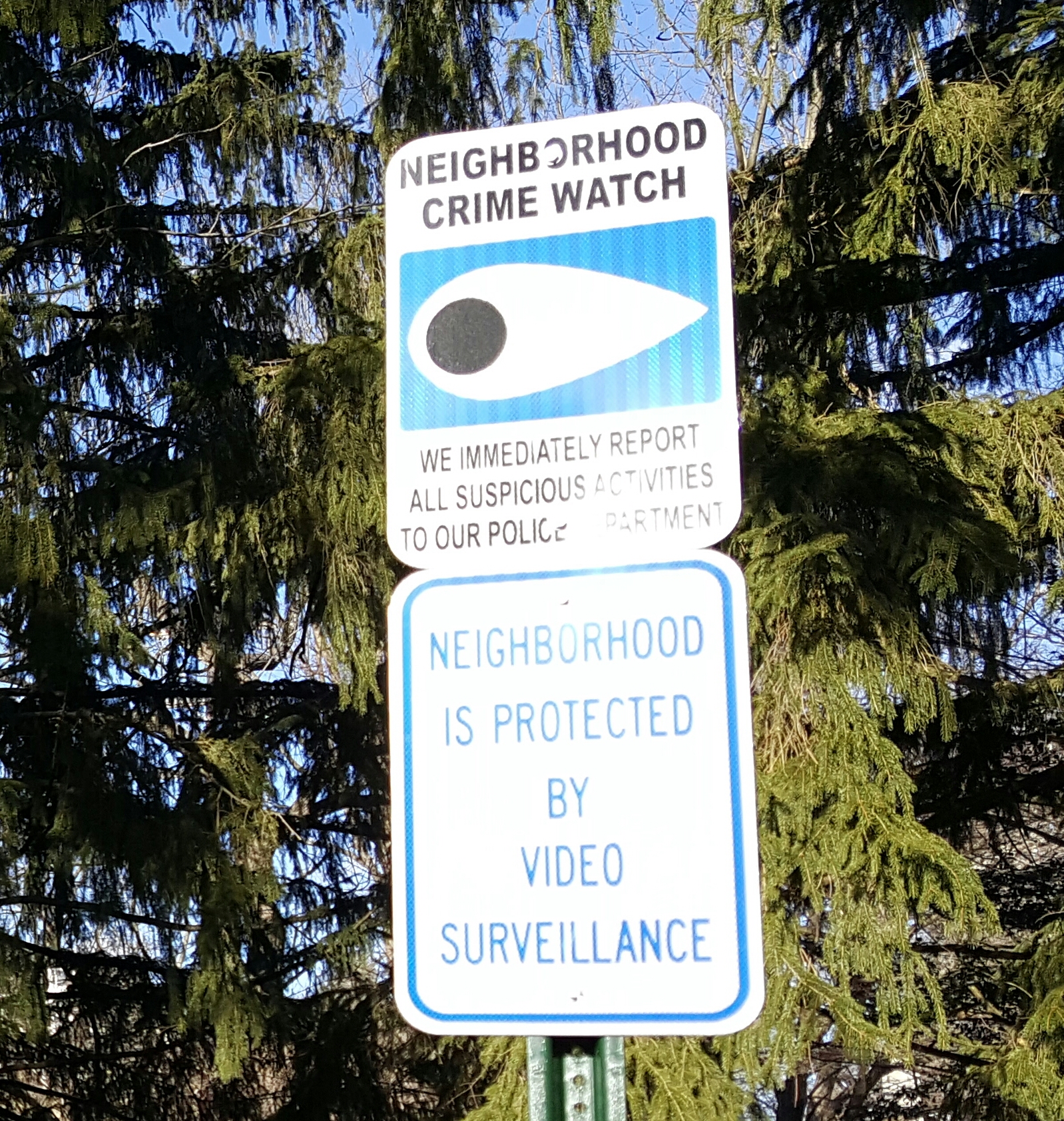 A neighborhood crime watch sign along Old Mill Road warns visitors that suspicious activity is reported to police and that the area is under video surveillance.