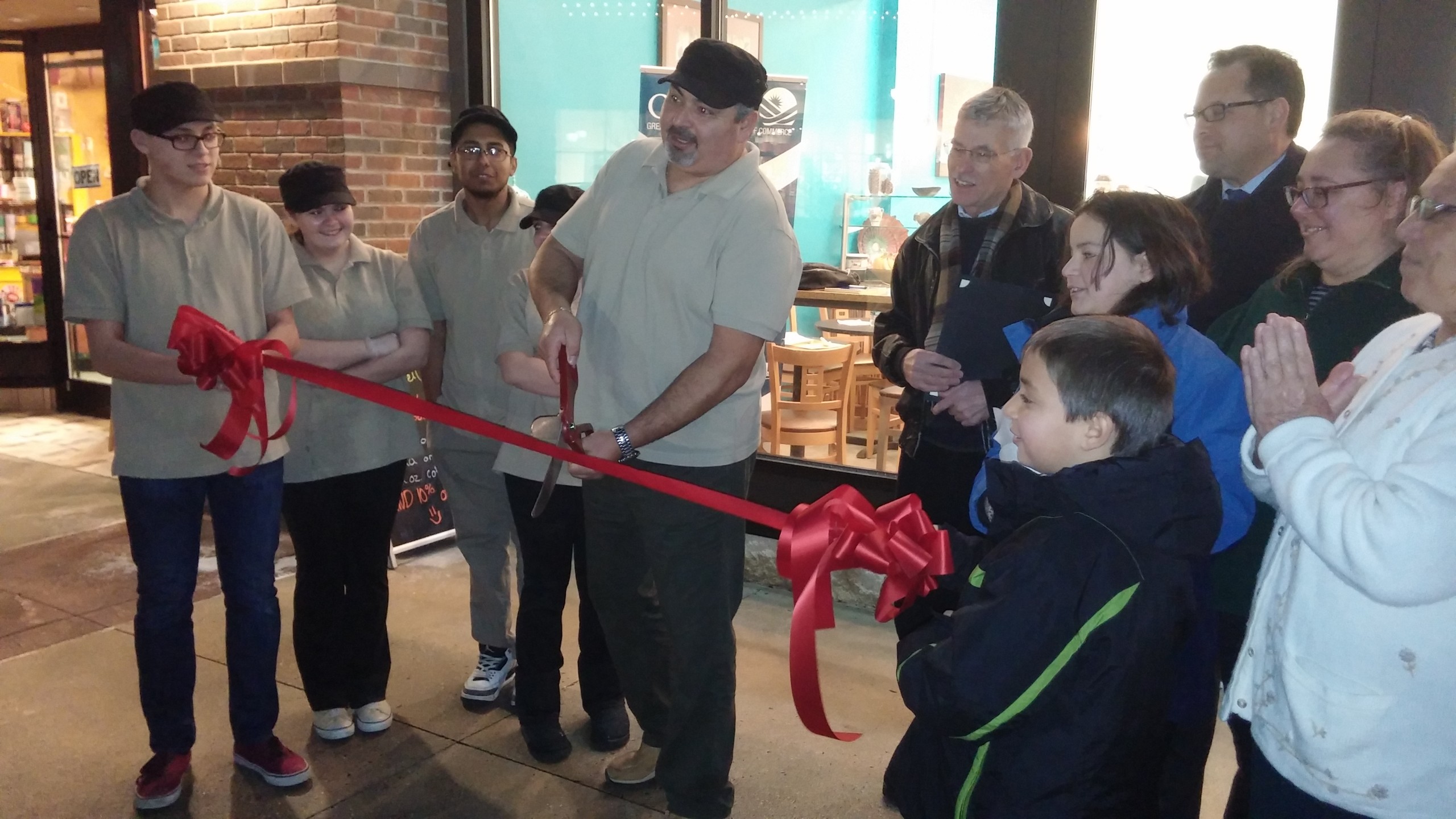 Crepe Soleil owner Seif Zaddem (center) cuts the ribbon in front of his new business at the Promenade Shops at Saucon Valley, as employees, family members and friends look on.